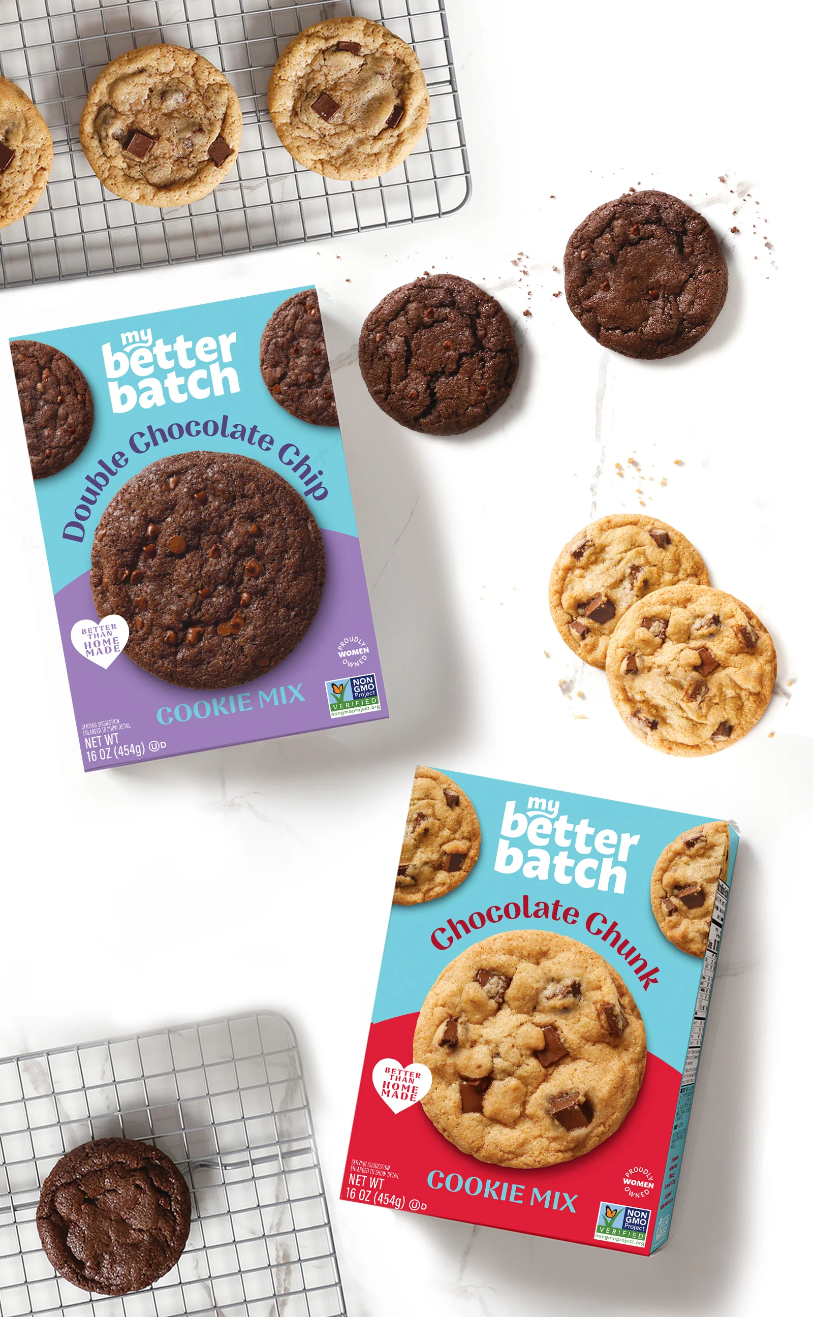 Two boxes of Gettrehouse cookie mix on a white marble surface with cookies placed around them. The Double Chocolate Chip box is purple, and the Chocolate Chunk box is red. Both boxes display images of the cookies along with branding and certifications. Some cookies are cooling on a wire rack.